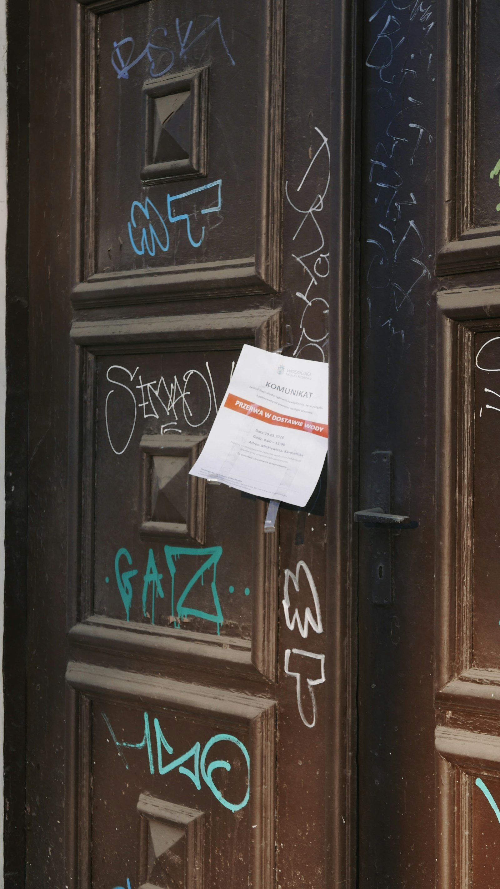 A heavily graffitied wooden door with a single small official notice taped near the handle.