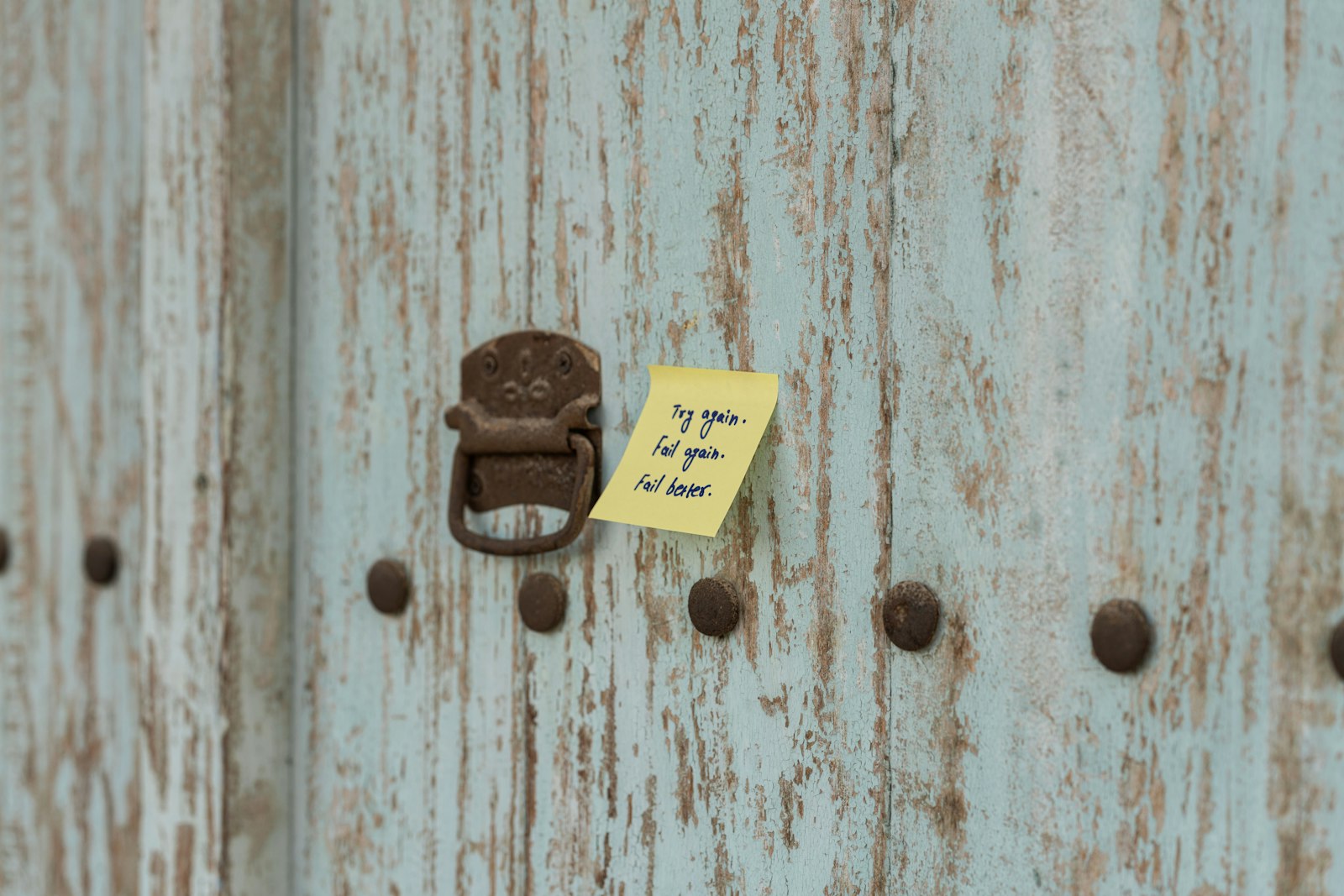 A small paper note pinned by a piece of clear tape to a battered door handle.